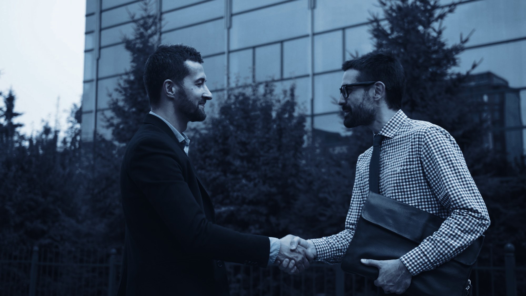 Two colleagues shaking hands outside a glass office building